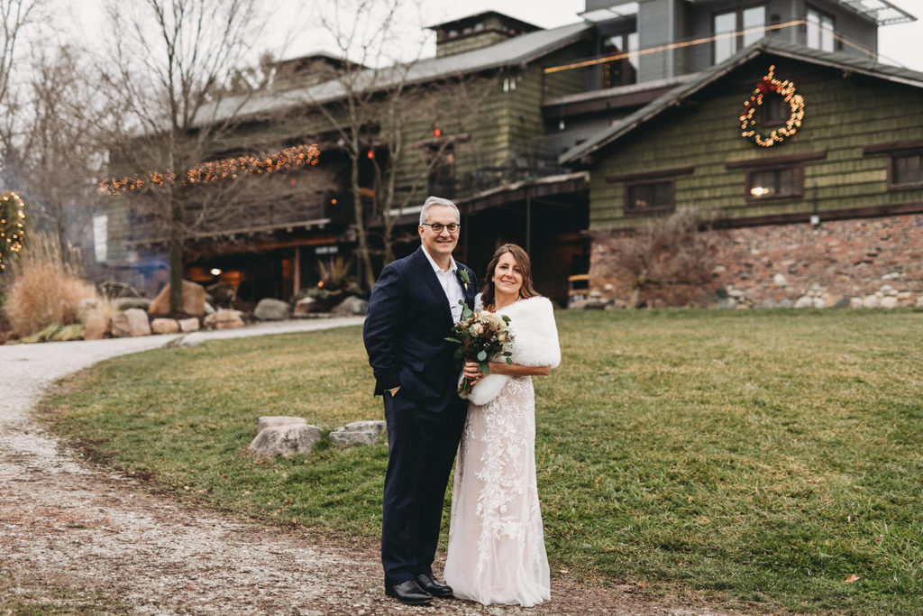 bride and groom stand in front of rustic building during their traders point creamery elopement