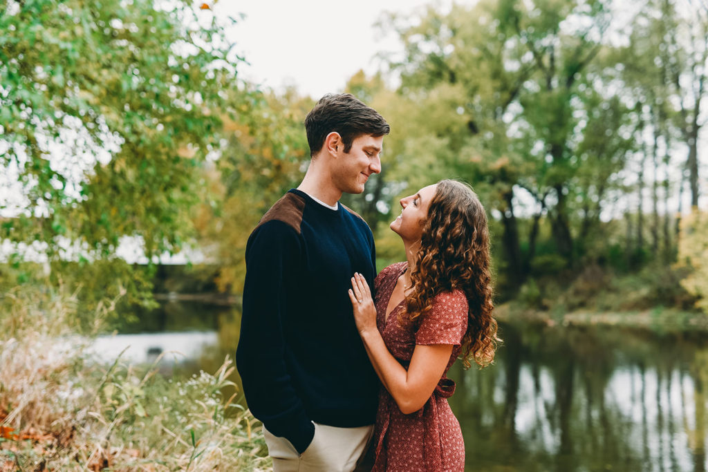 couple embrace on banks of White River in Noblesville during their Potters Bridge Engagement session