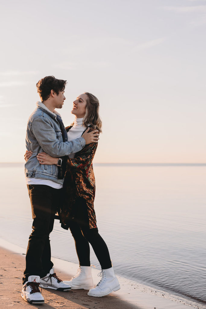 man and woman huge next to completely still lake michigan during their Indiana Dunes engagement photos
