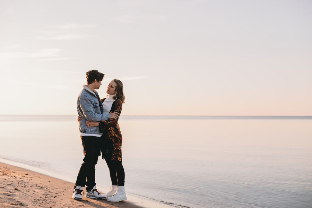 man holds woman in passionate embrace on the shore of Lake Michigan during their Indiana Dunes engagement photos