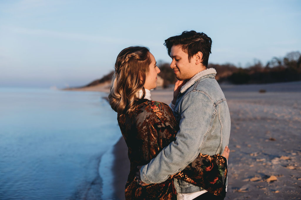 young couple hug and look lovingly into each other's eyes on the shore of lake michigan at an Indiana National Park