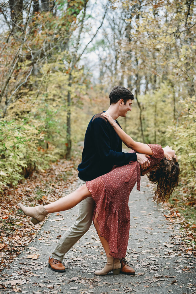 man dips woman on trail surrounded by fallen leaves during their Potters Bridge Engagement session