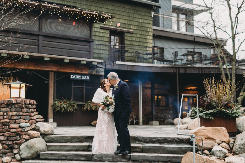bride and groom kiss in front of rustic building during their traders point creamery elopement