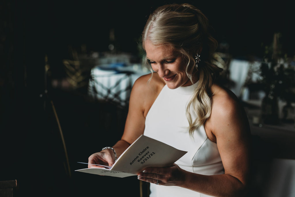 blonde bride reads letter in dark and moody window light before her indy canal wedding