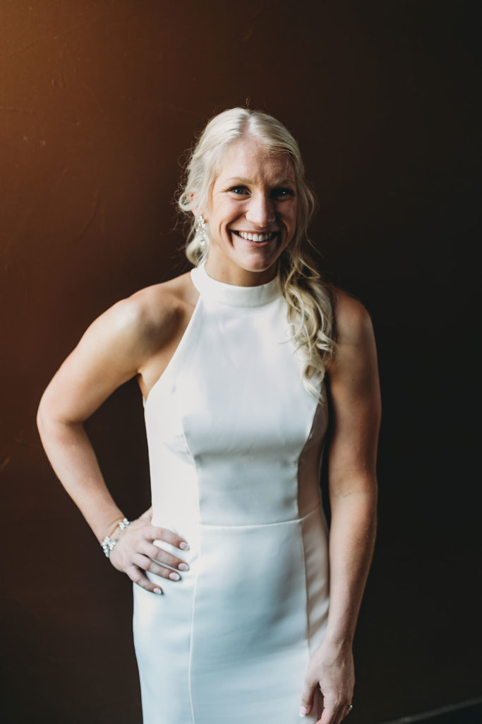 blonde bride smiles in front of brown wall at her indy canal wedding