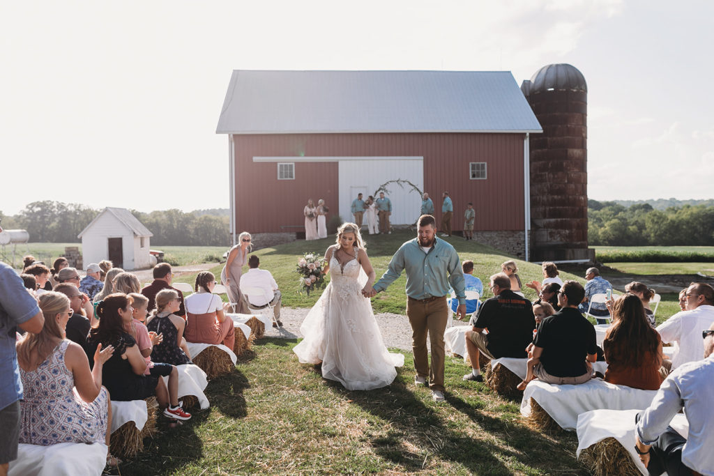 bride and groom walk away from red barn holding hands at one of the Best Indianapolis Barn Venues