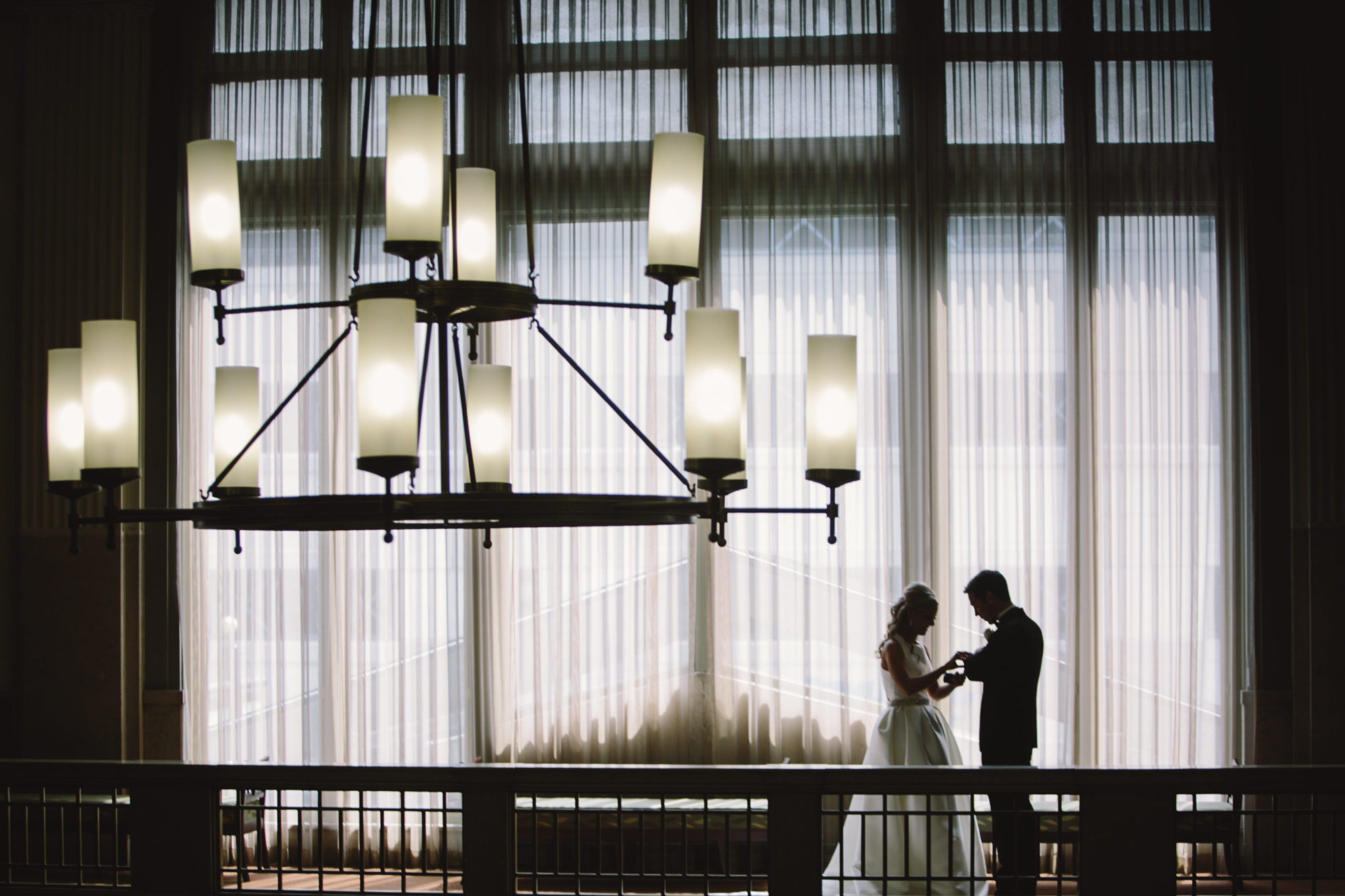 the silhouette of a bride and groom in front of large windows at the Hilton Garden Inn in downtown indianapolis with a large chandelier hanging in the foreground