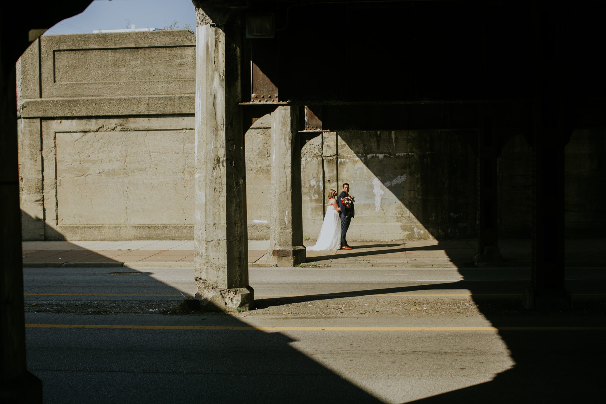 a bride and groom stand in a triangle of light under a bridge in downtown indianapolis on their wedding day