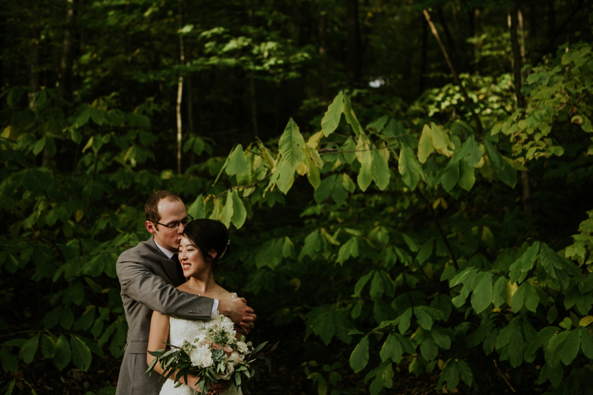 a bride and groom hug and kiss in front of large, tropical, green leaves surprisingly growing in happy hollow park in lafayette