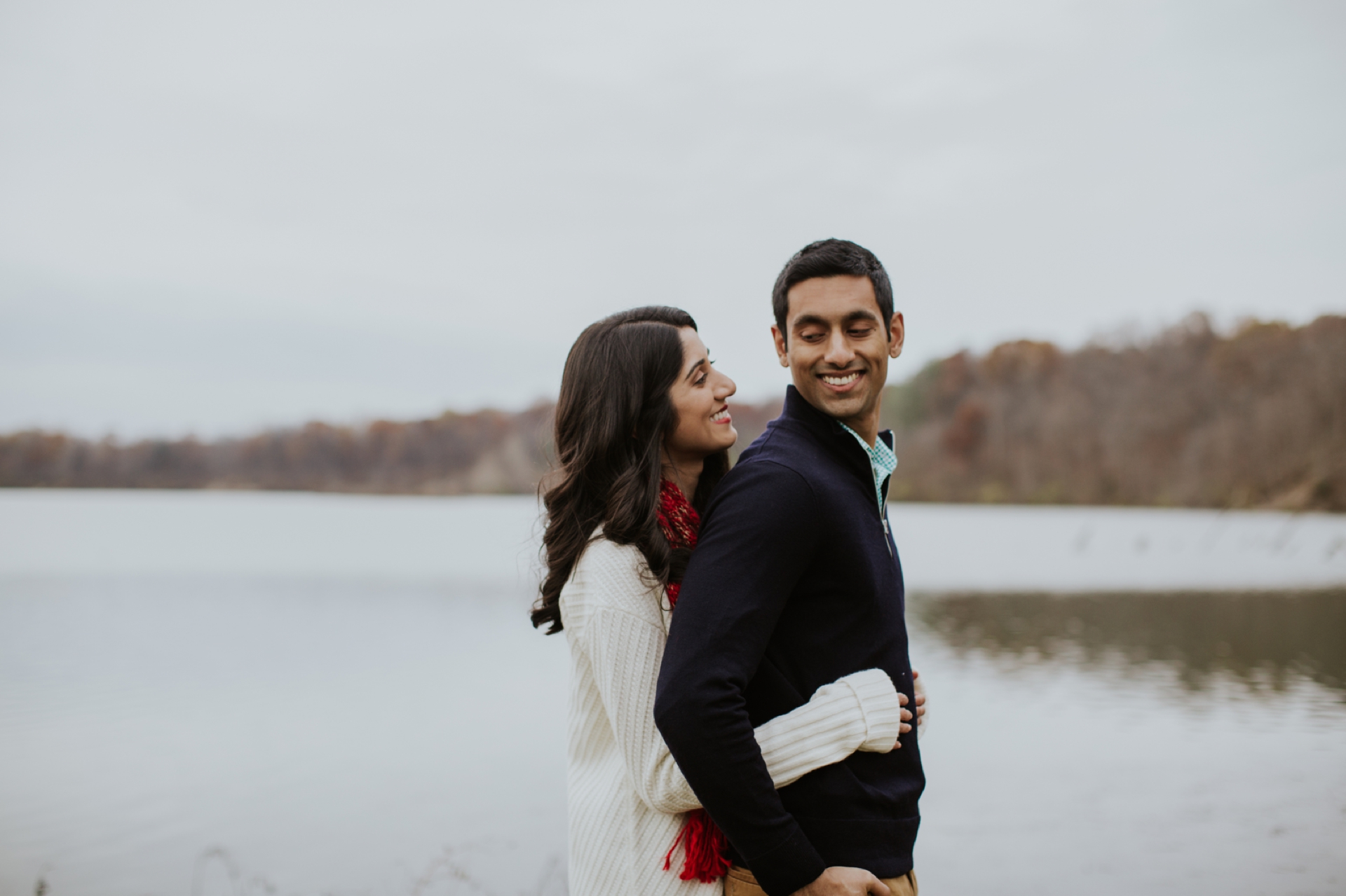 a man and woman with black hair stand on the side of the reservoir hugging at their eagle creek engagement session