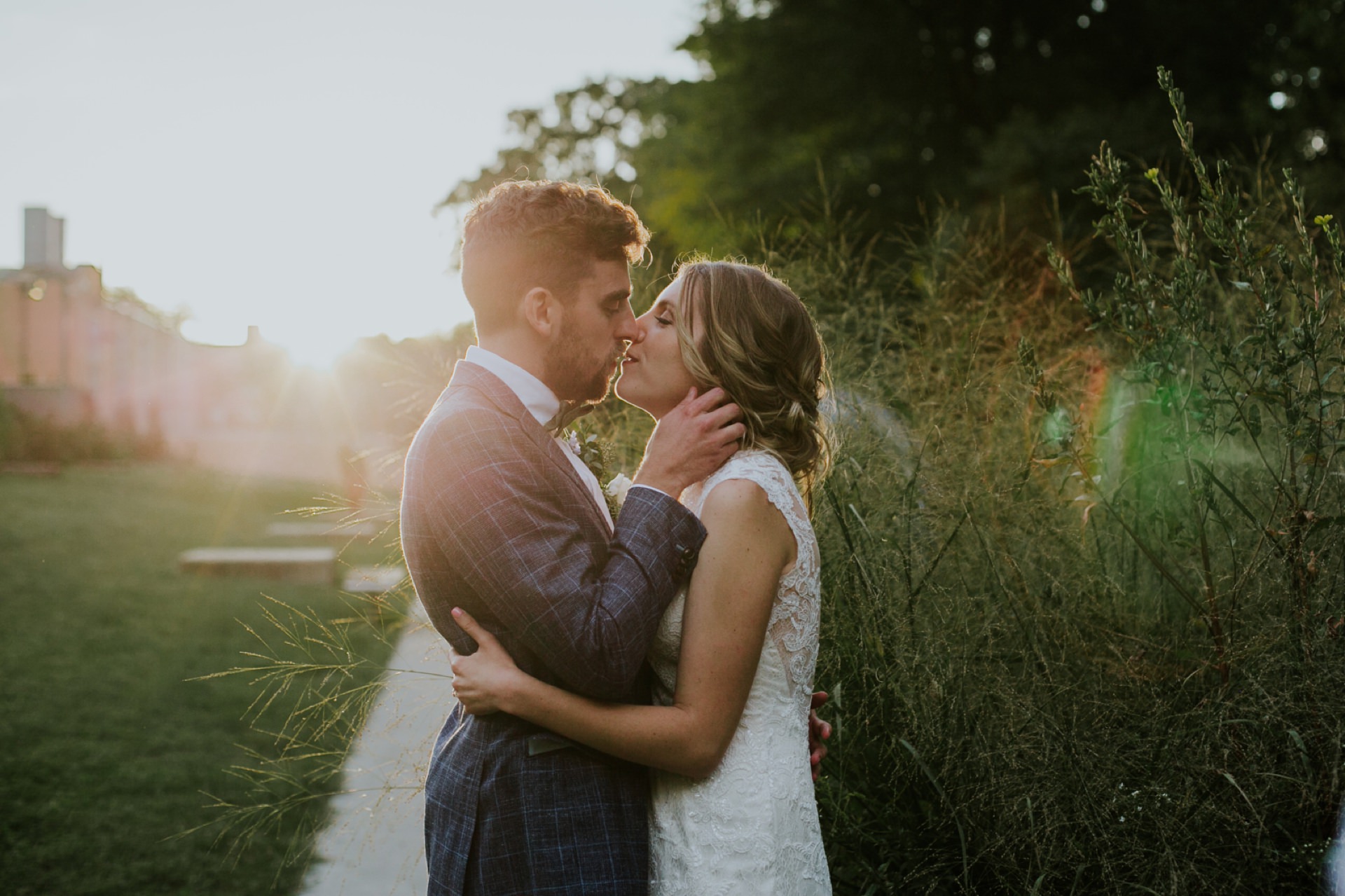 dapper groom and beautiful bride kiss at sunset with beautiful flares in frame at their indianapolis art center wedding