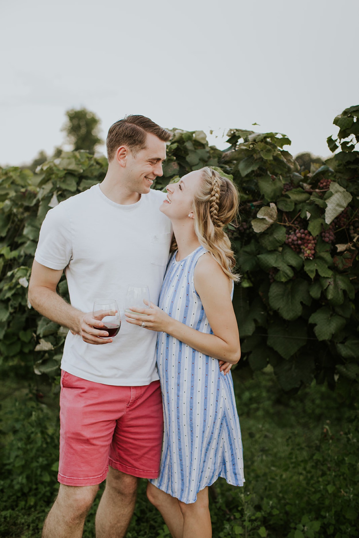 a man and a woman stand in a vineyard drinking glasses of wine in this vineyard publication shoot
