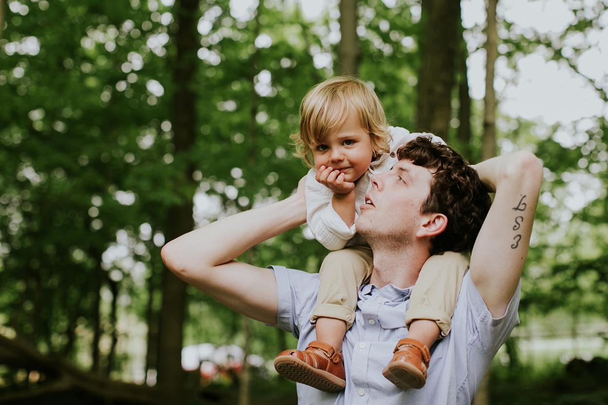 man with tattoo looks up at son on his shoulders in this cool creek family photography session