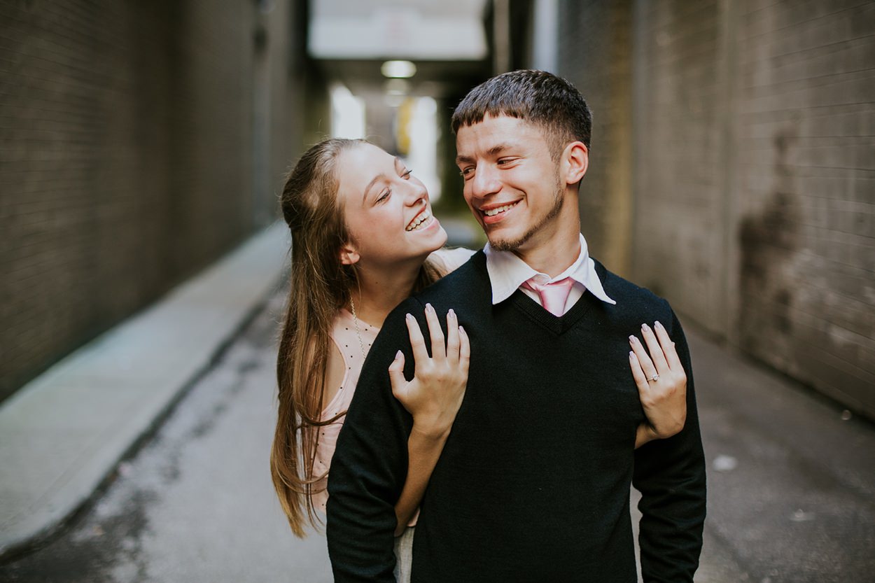 a woman hugs a man from behind and he turns his head to look at her during their downtown indianapolis engagement photography