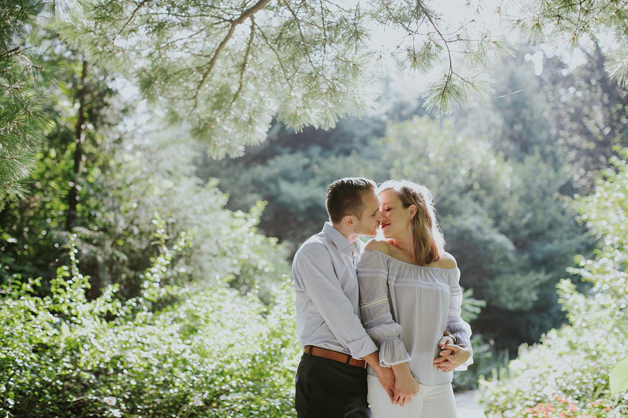 A man and woman in nice clothes kiss in the middle of some trees during their Newfields Engagement session