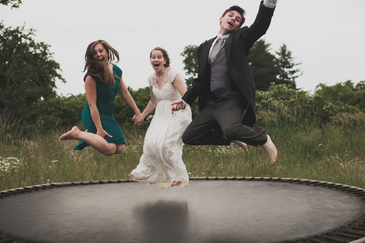 behind the scenes photo of a photographer jumping on a trampoline with a bride and groom