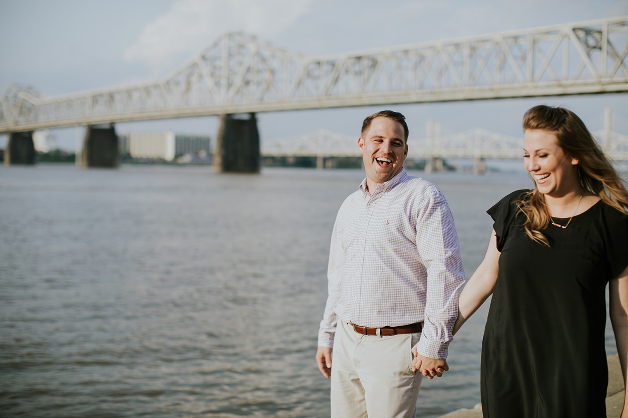 couple stands on the banks of the river laughing and holding hands during their downtown Louisville engagement session