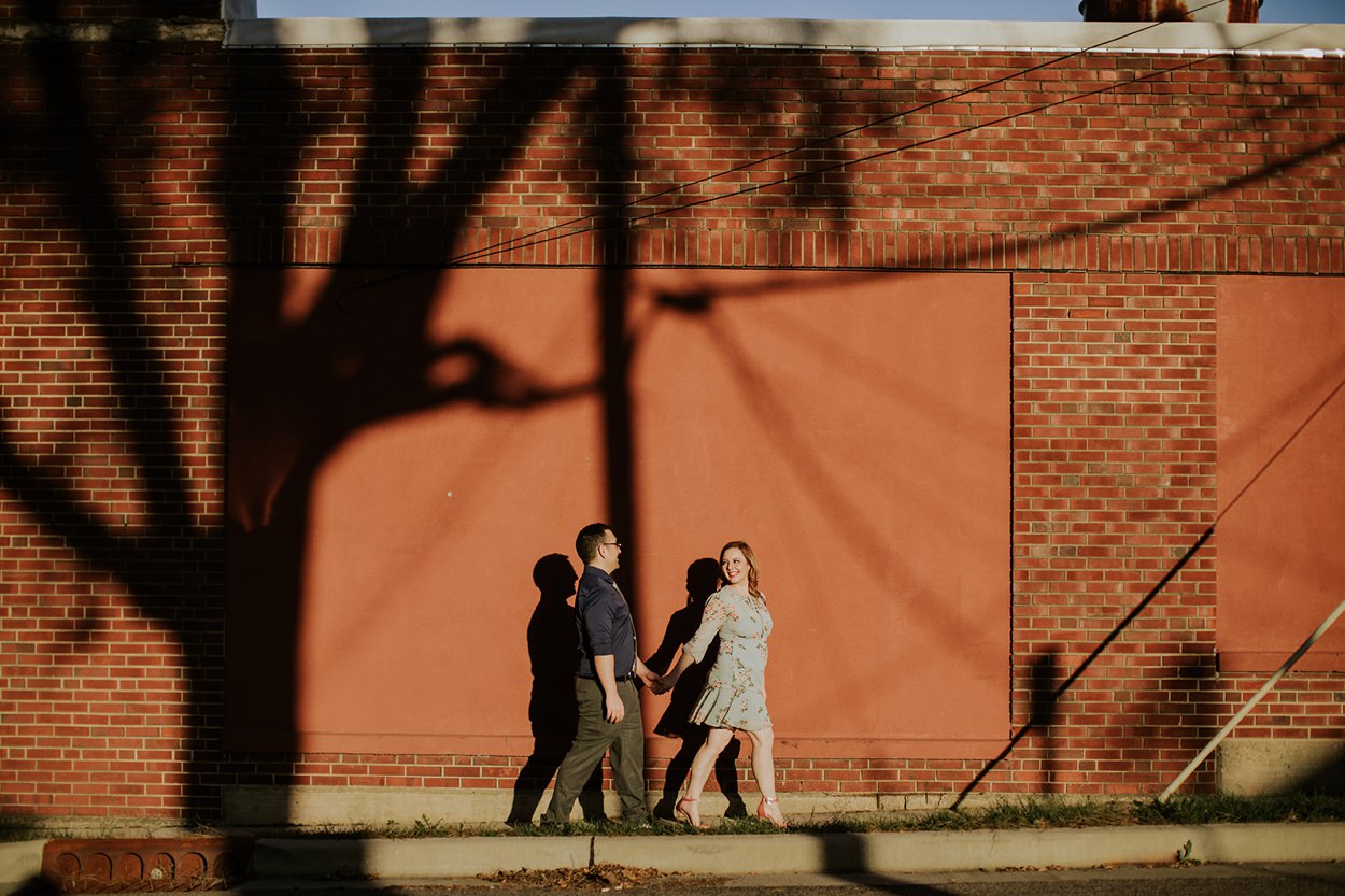a man and woman walk in front of a brick wall in their goshen engagement photography session