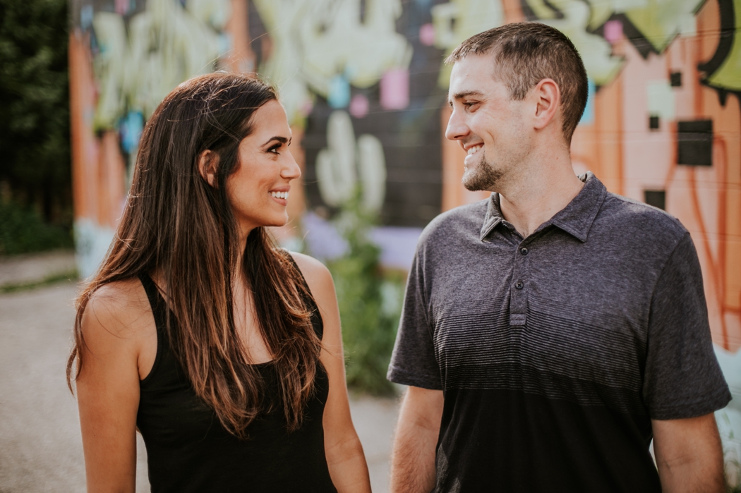 man and woman hold hands and smile in front of graffiti during their fountain square engagement shoot
