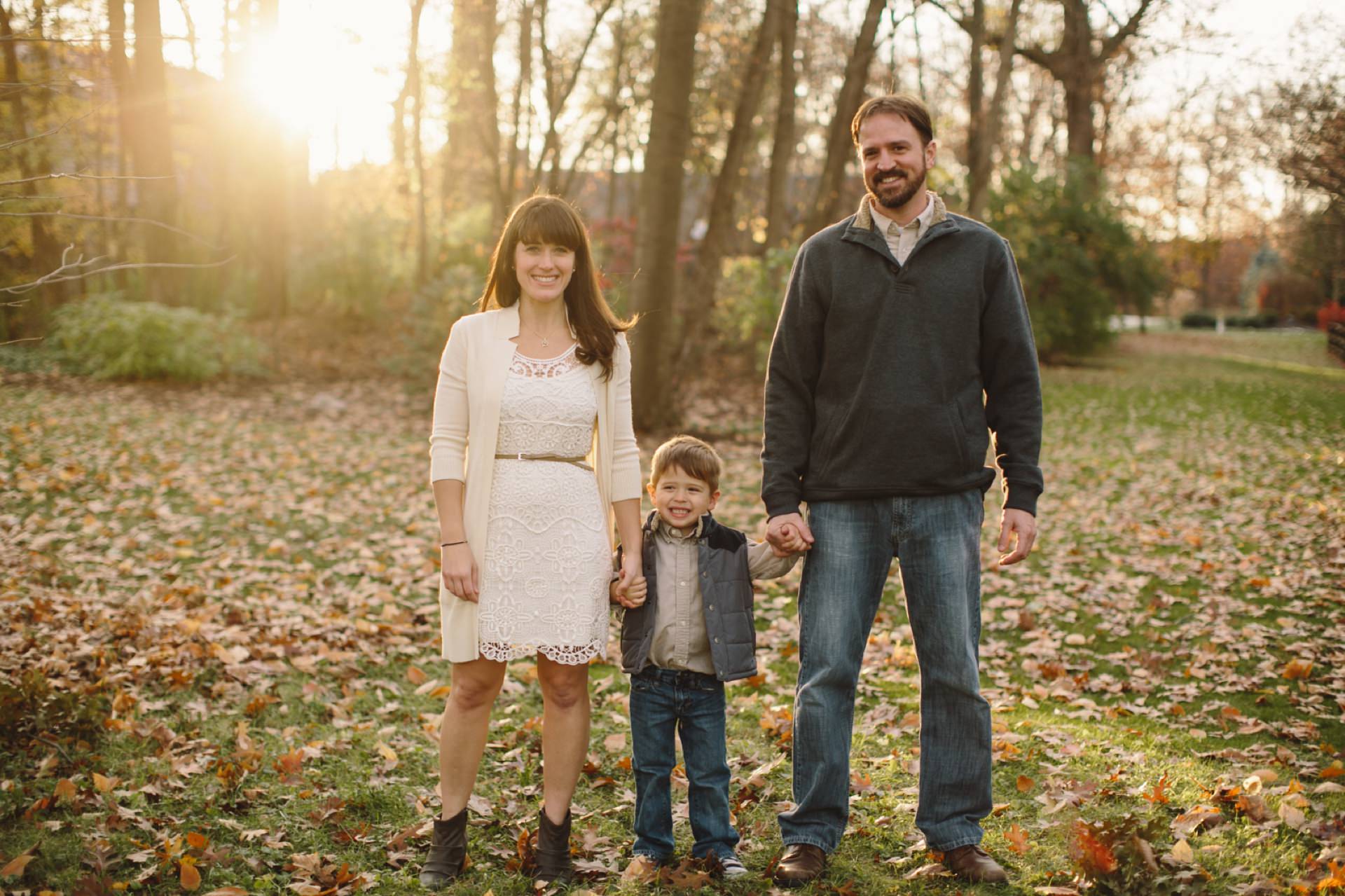 mom, dad, and son stand amidst crisp autumn leaves holding hands at sunset for their Fishers Family Photos