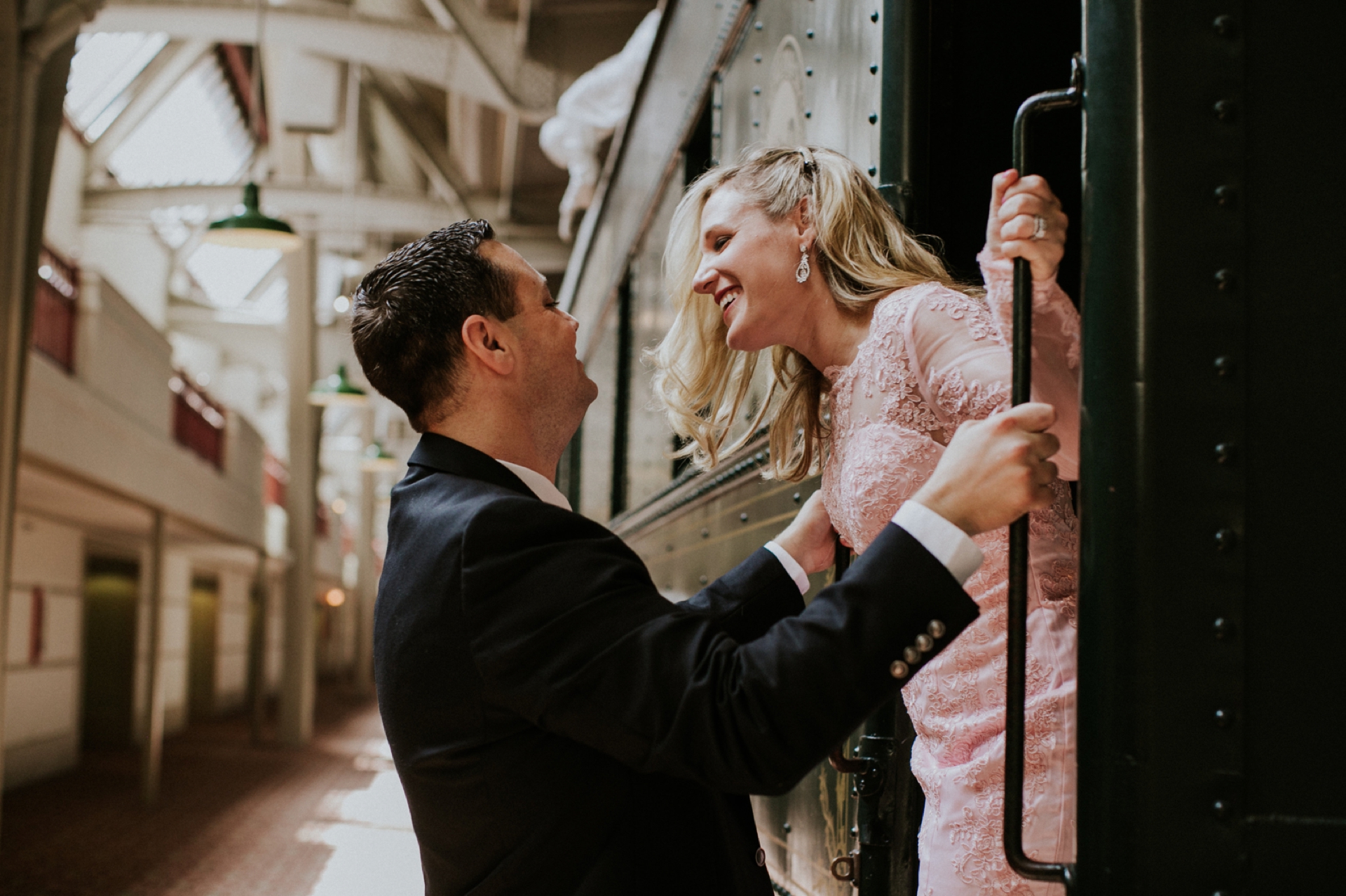 blonde woman in white dress standing in the doorway of a train looks lovingly at man in suit during their crowne plaza union station family photos