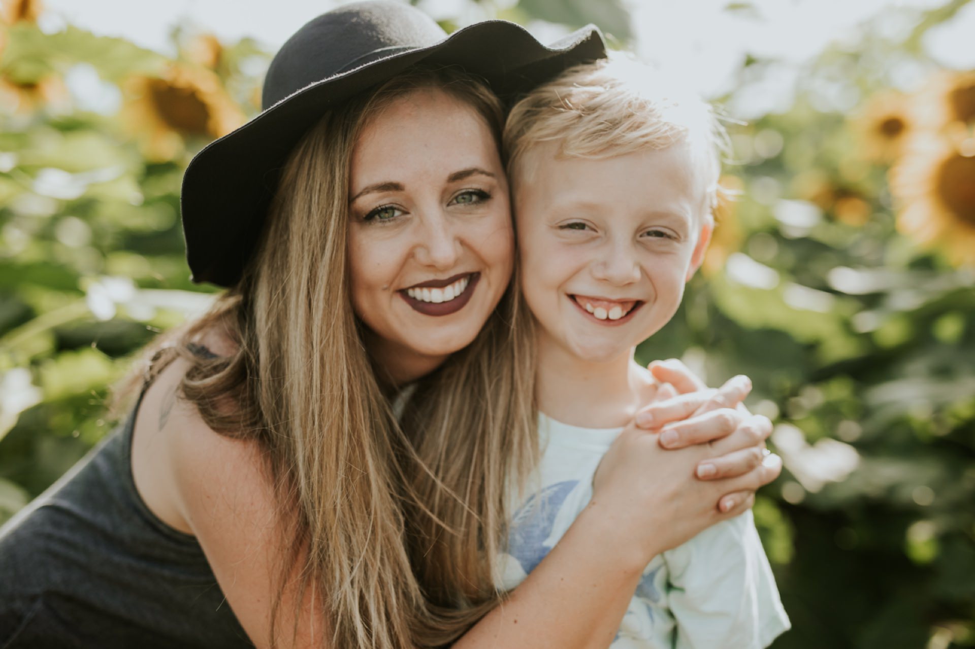 beautiful woman in hat hugs son in sunflower pictures at tuttle orchard