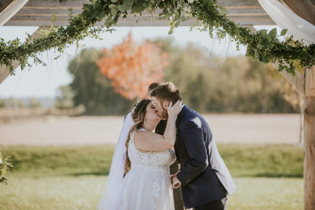 bride and groom share first kiss at zyntango farms under greenery at one of the Best Indianapolis Barn Venues