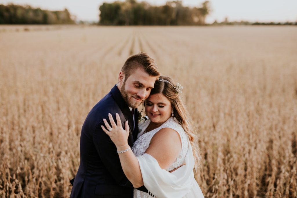 a newly married couple hugs in front of a field of soy beans at this zyntango farm wedding one of the Best Indianapolis Barn Venues