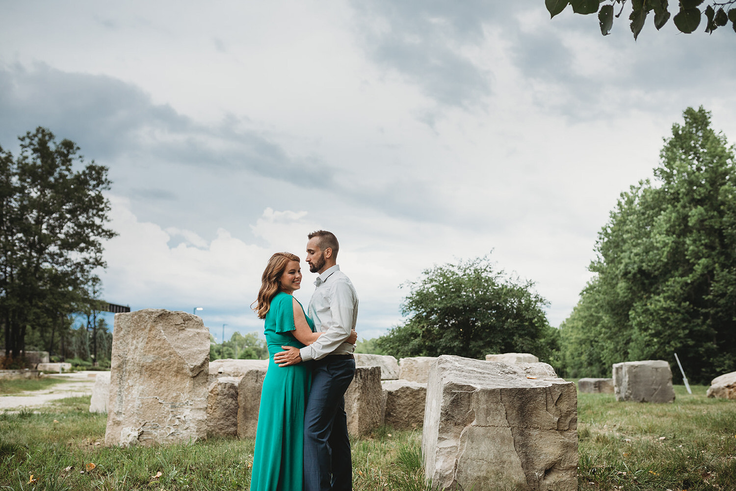 woman in green dress and man in blue pants hug in front of rocks during their bloomington engagement session