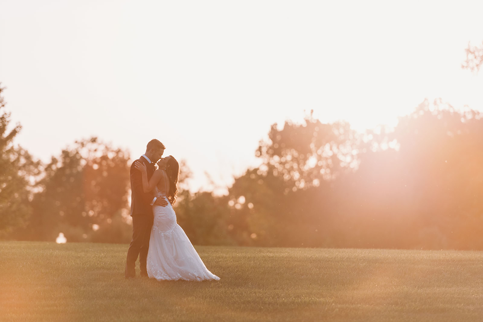 bride and groom hug and kiss in open field at sunset during their Carmel Backyard Wedding