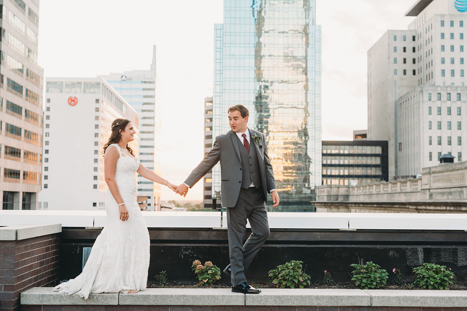 man and woman in wedding attire hold hands and walk along edge of building during their regions tower wedding celebration