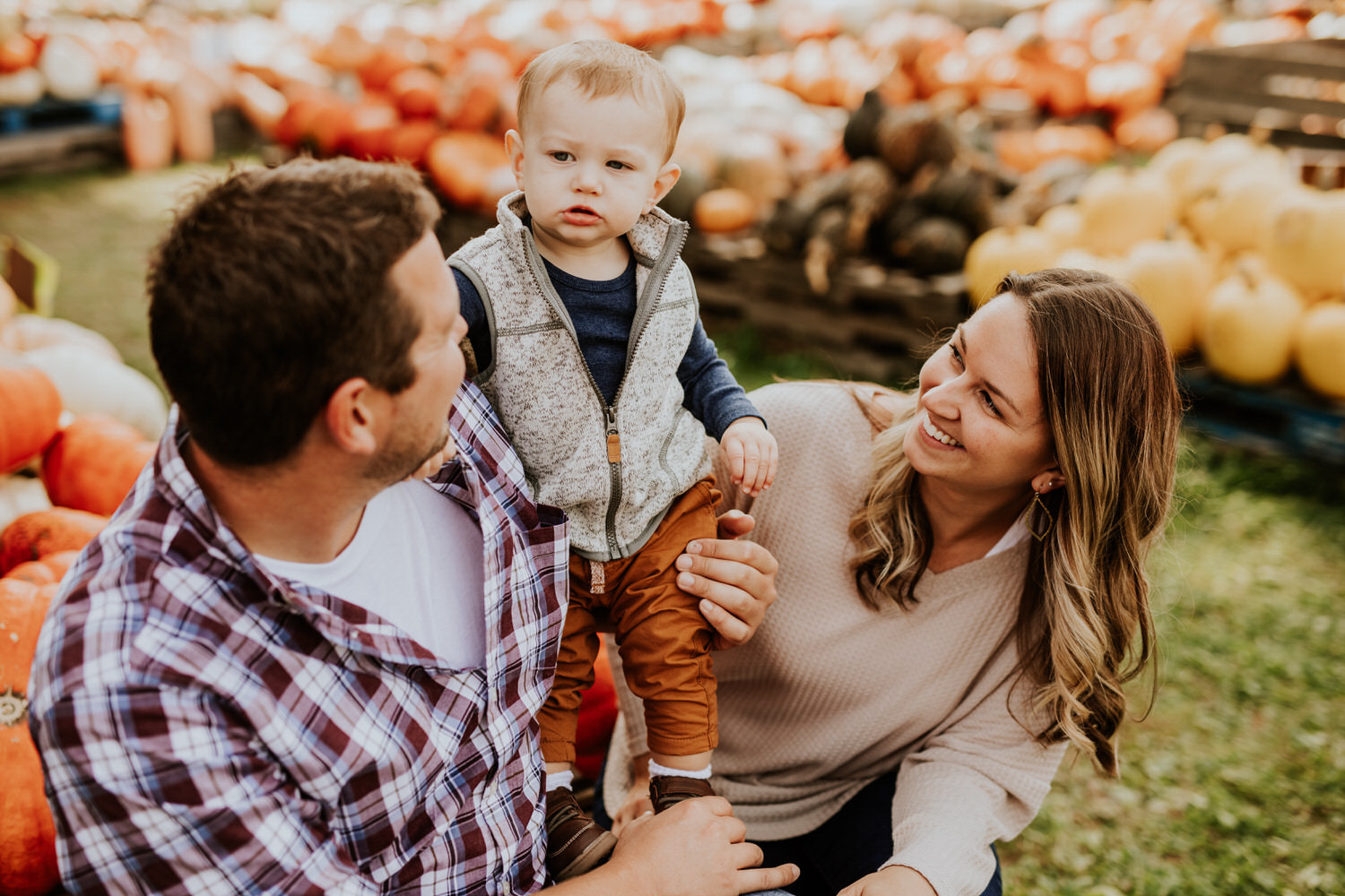 mom and dad smile with baby in pumpkin patch during their Russell Farms Family Photos