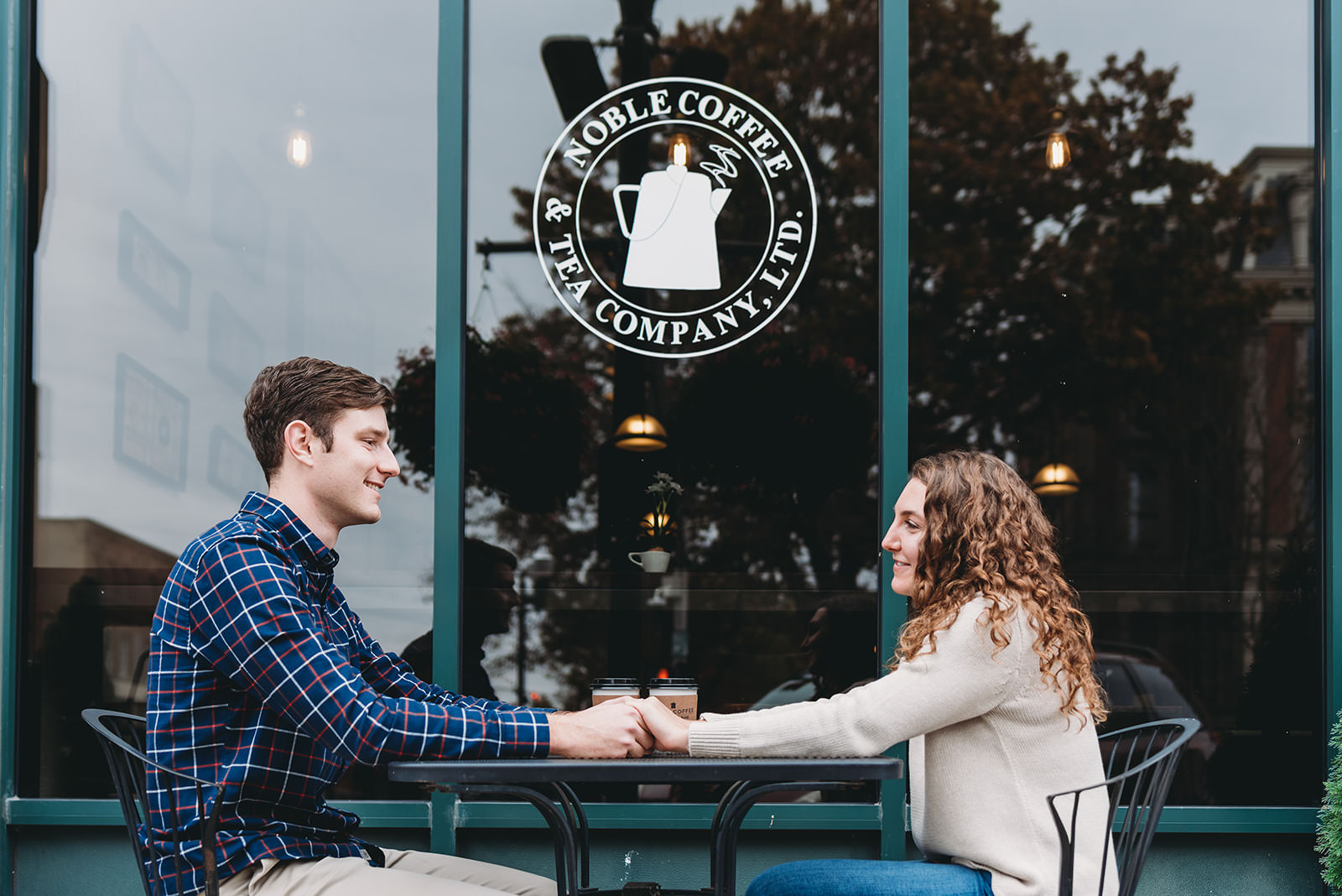 young couple holds hands at a table outside of Noble Coffee and Tea Company in Noblesville