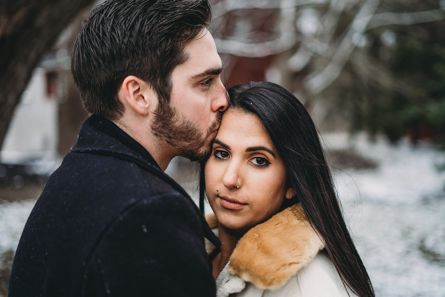 man with beard kisses woman on head on snowy day during their mustard seed gardens engagement photos