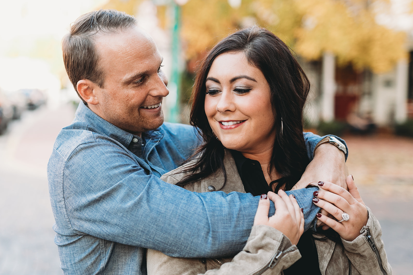 man hugs woman in front of autumnal background during their downtown zionsville engagement session
