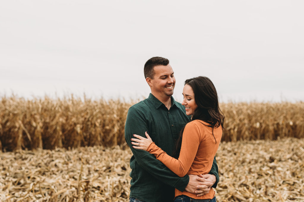 husband and wife hug in half harvested corn field during this Central Indiana Family Photography session