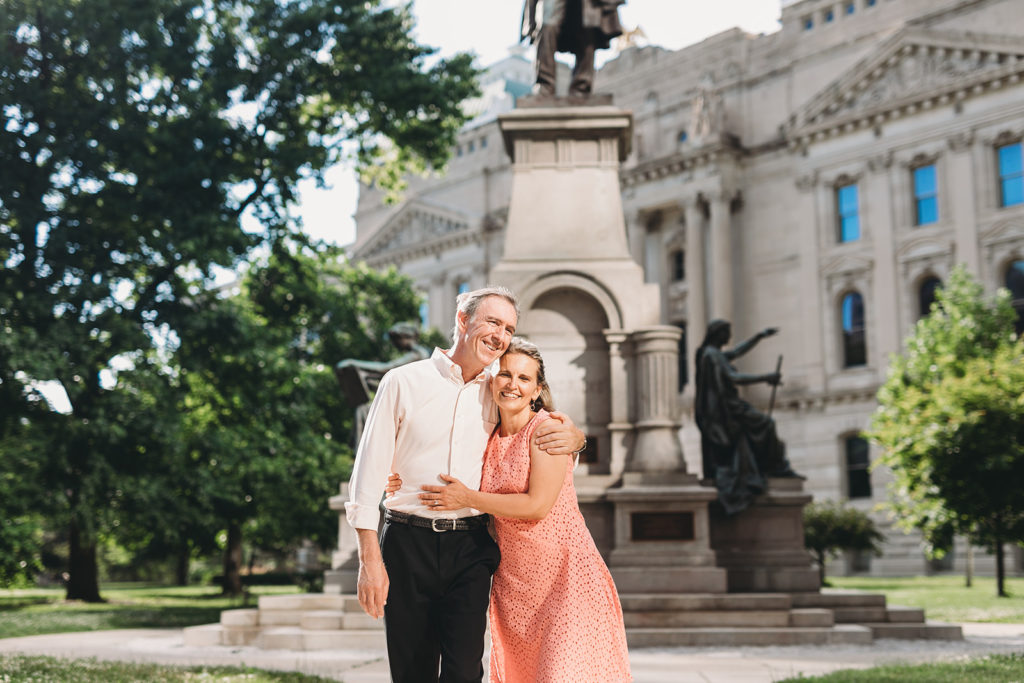man and woman side hug in front of the Indiana statehouse during their Indianapolis Canalwalk engagement session