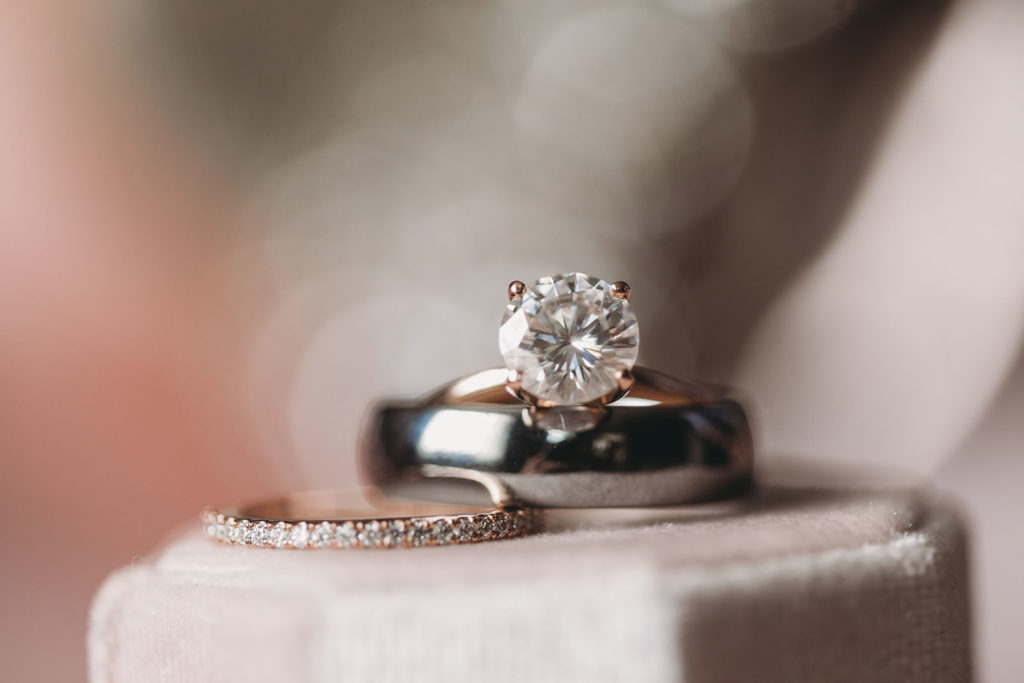 engagement ring with lots of bokeh behind it and sitting on top of wedding rings on top of bink box
