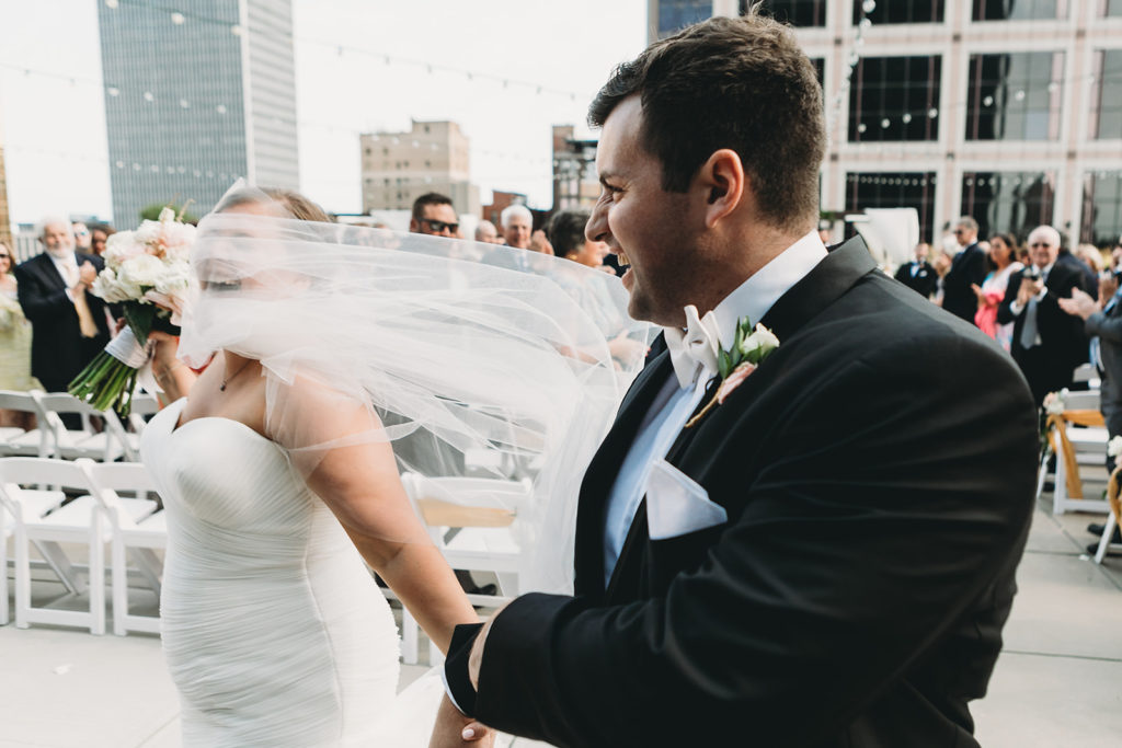 bride's veil blows into her face as she leaves the ceremony causing her to laugh at her Charming Regions Tower Wedding