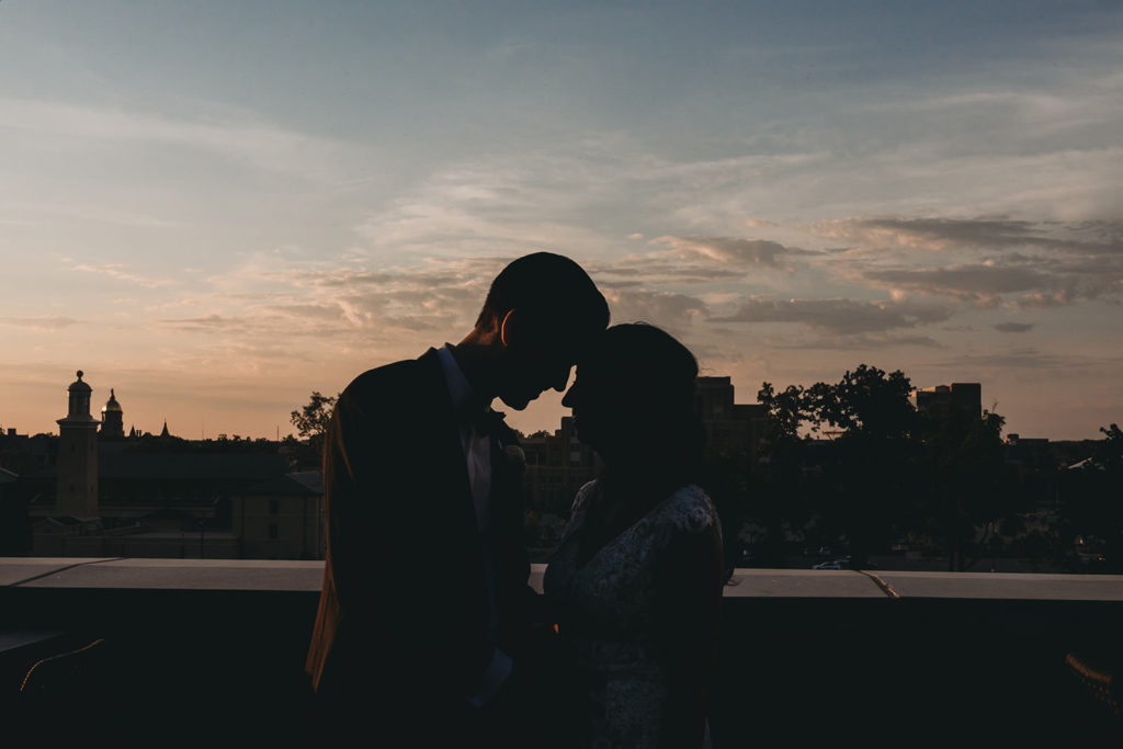 bride and groom silhouetted touching foreheads at sunset at the Embassy Suites in south bend's rooftop bar during their Notre Dame Wedding