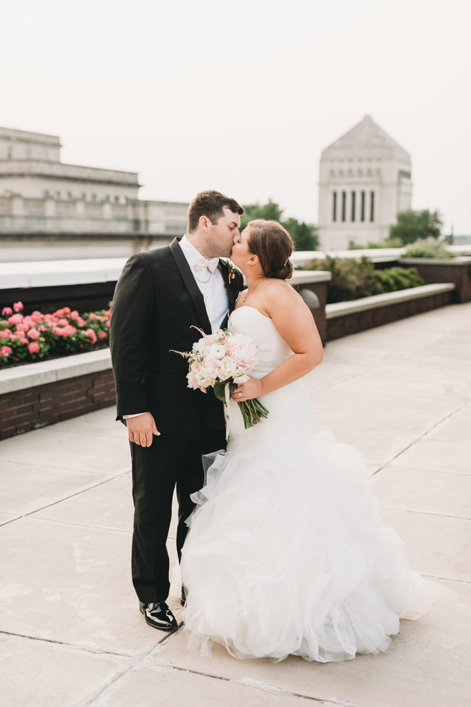 bride and groom kiss on terrace of regions tower during with indiana war memorial building in the background during their Charming Regions Tower Wedding