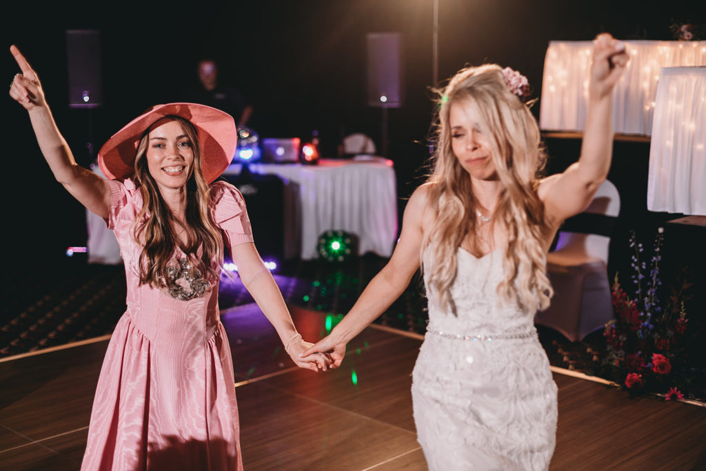 The bride and a bridesmaid dance on the dance floor, the bridesmaid wearing a replica of one of the ugly bridesmaid dresses from the television show FRIENDS in these unique wedding photos