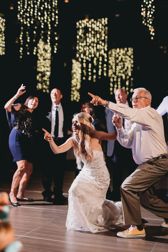 Wedding guests dancing at on the dance floor point to someone off frame excitingly.