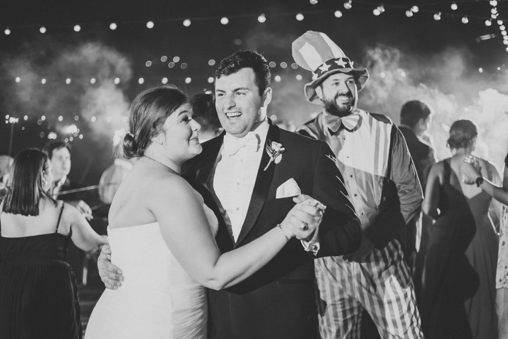bride and groom dance while man dressed as uncle sam dances behind them and their guests wave sparklers in the air during this Charming Regions Tower Wedding