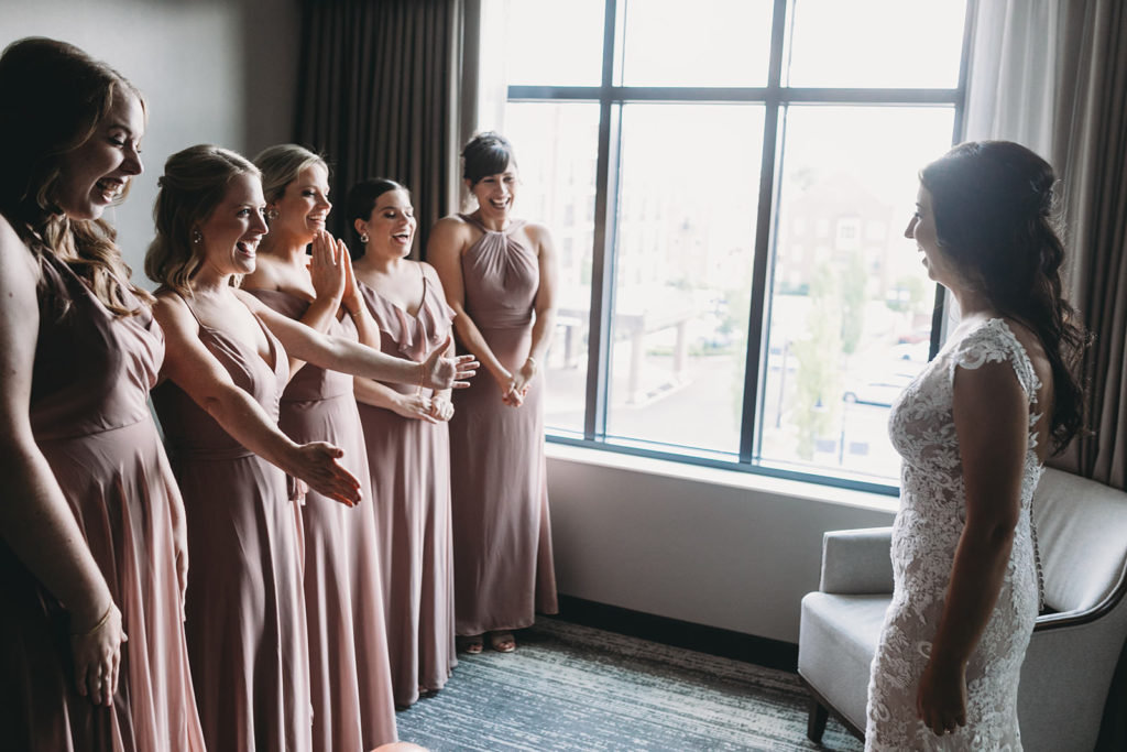 bride smiling as bridesmaids in pink dresses see her in her wedding dress