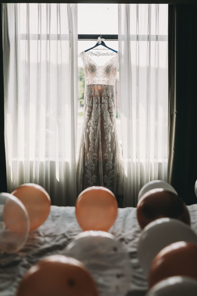 wedding dress hanging in window behind behind bed covered in balloons at embassy suites in south bend