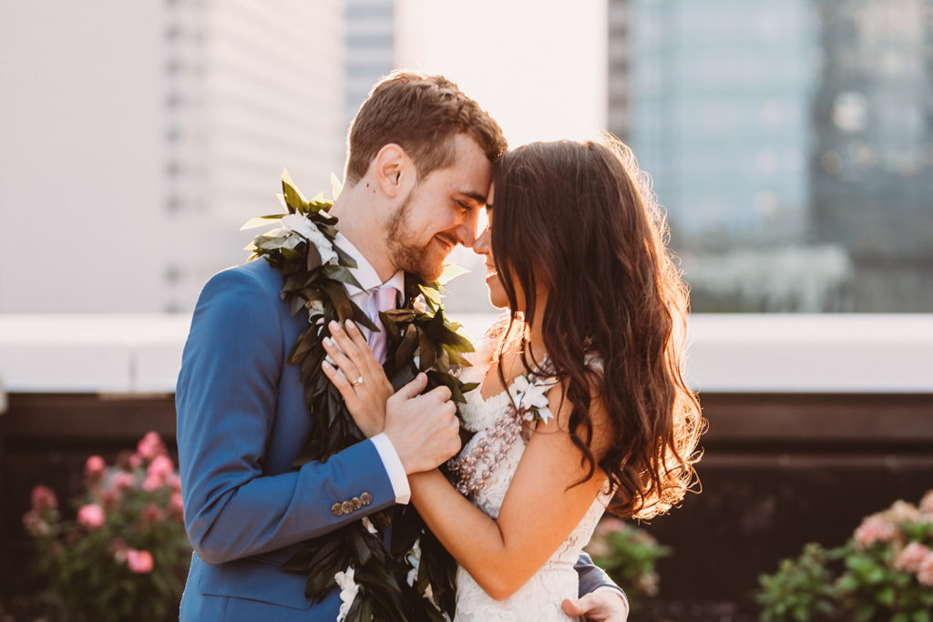 bride and groom touch foreheads while hugging and wearing leis at their groom in blue suit dips bride in white dress and kisses her at sunset at their Indianapolis Hawaiian Jewish wedding