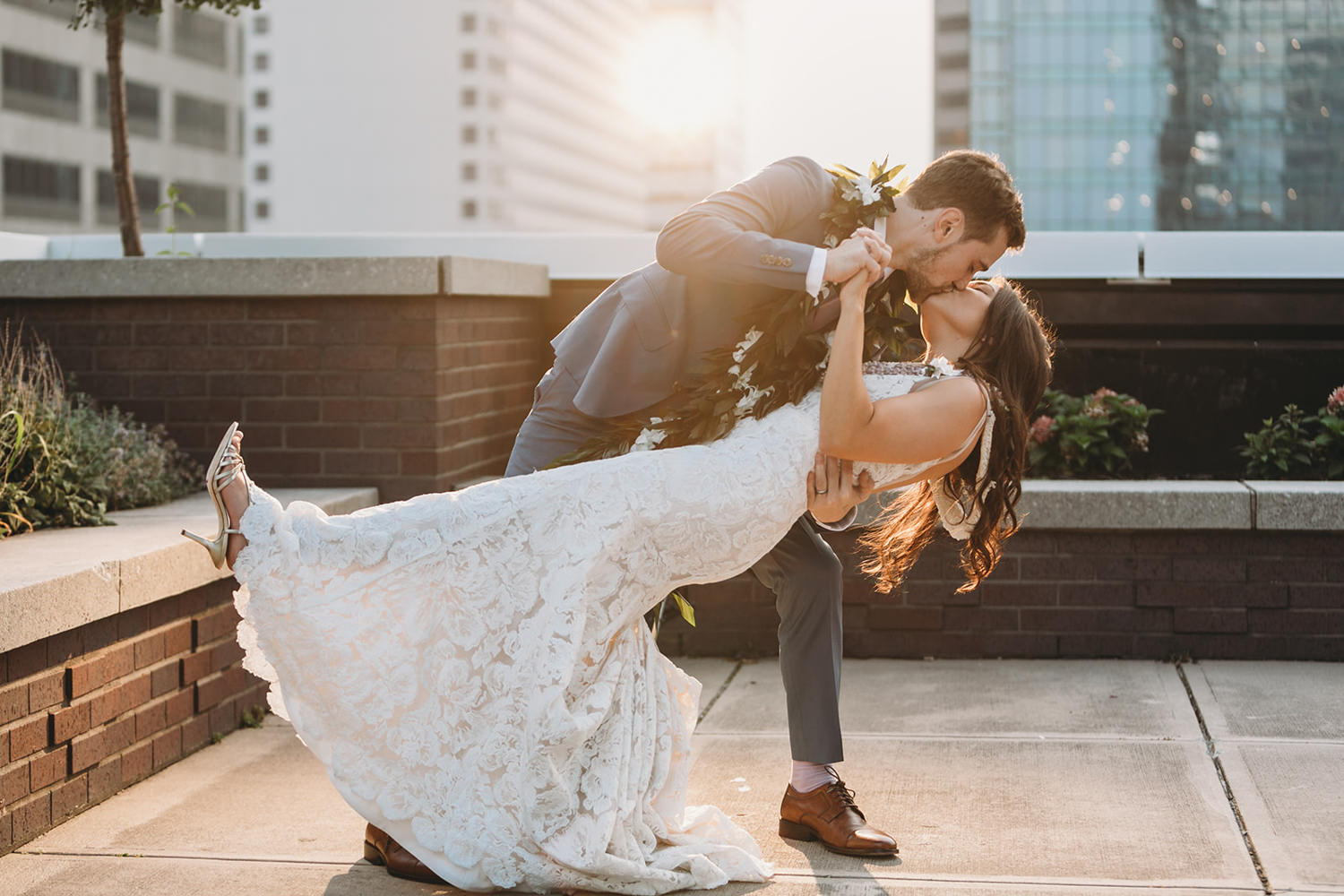 groom in blue suit dips bride in white dress and kisses her at sunset at their Indianapolis Hawaiian Jewish wedding