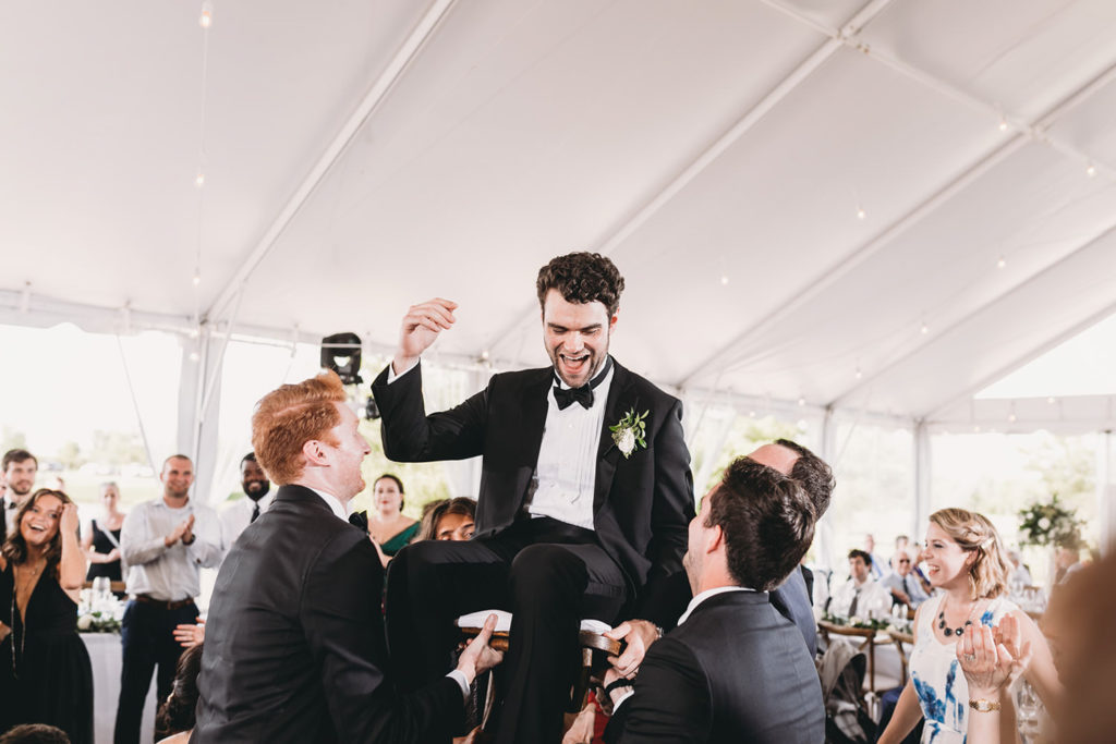 guests lift groom high into the air during the Horah at his charming coxhall gardens wedding