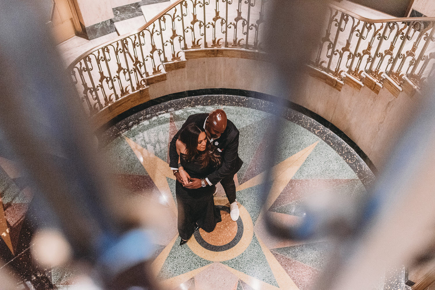 man and woman hug on top of star floor at bottom of circular stairs during their bottleworks engagement session